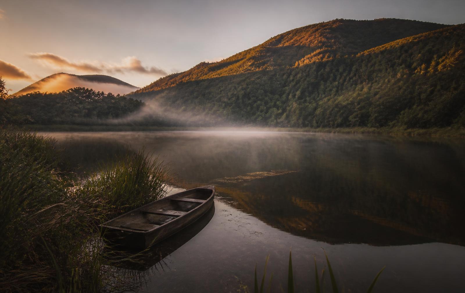Laguna de La Cocha al amanecer, con niebla sobre el agua y una canoa de madera